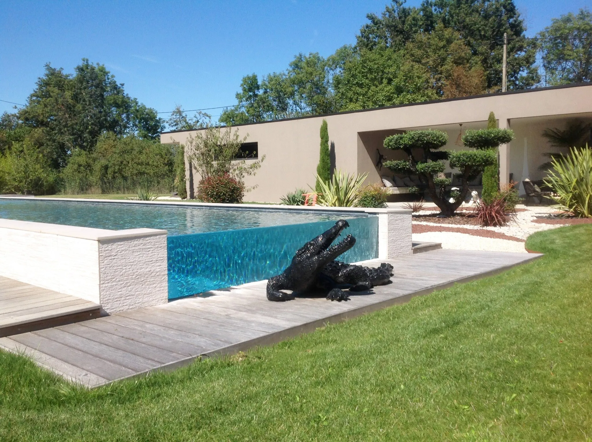 Piscine miroir bordée d’une terrasse en bois et d’un jardin