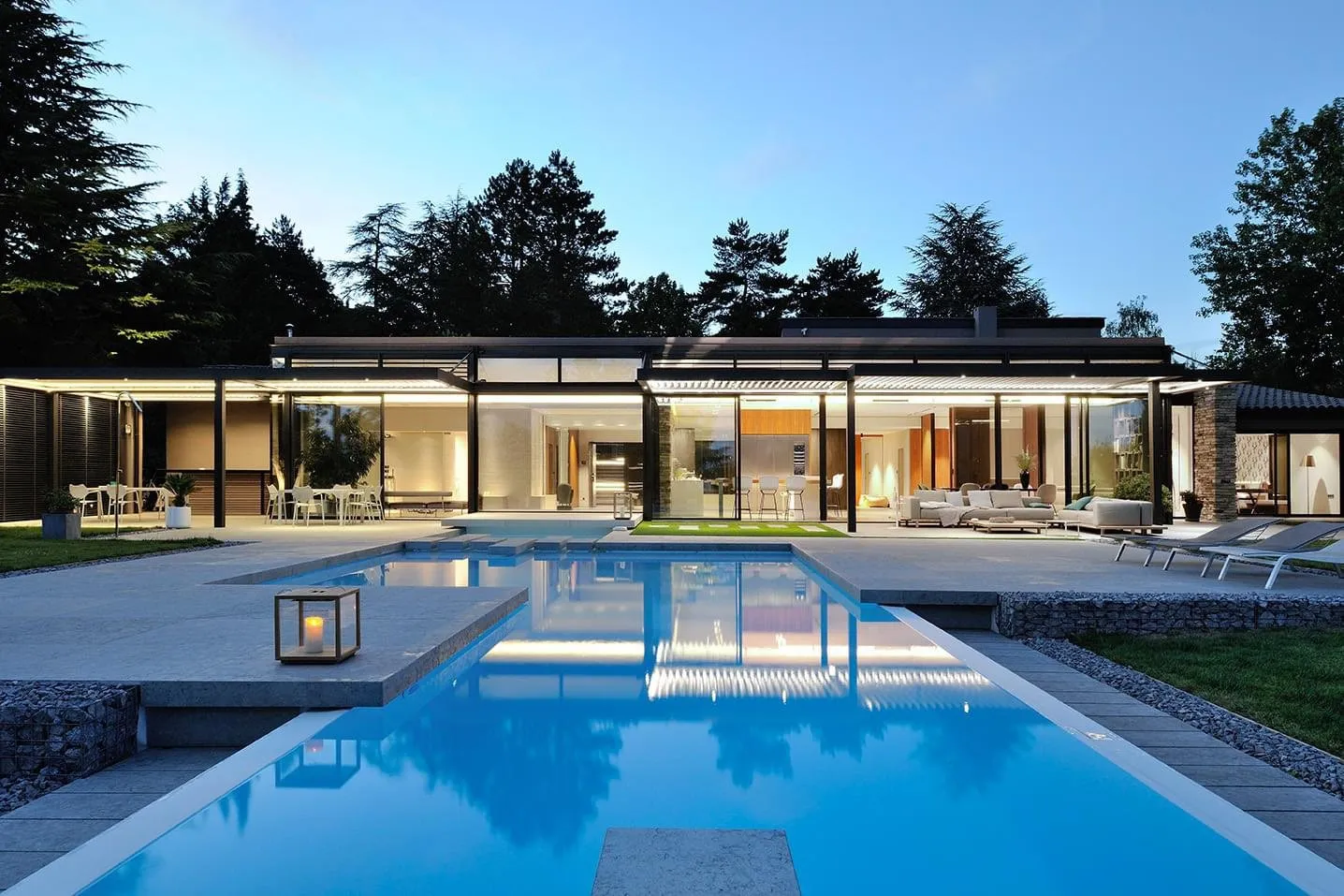 Piscine au crépuscule devant une maison vitrée